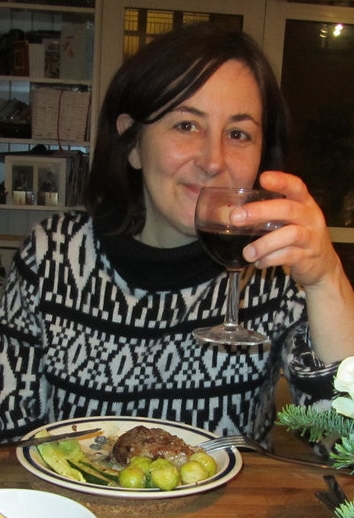 Eleanor smiling holding a glass of red wine, she has a plate of food in front of her. Shes wearing a black and white jumper.