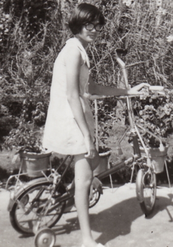 black and white photo of girl on bike with glasses. shes wering a dress.