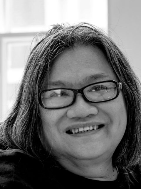 East Asian women with greying hair with dark rimmed glasses smiling - black and white photo